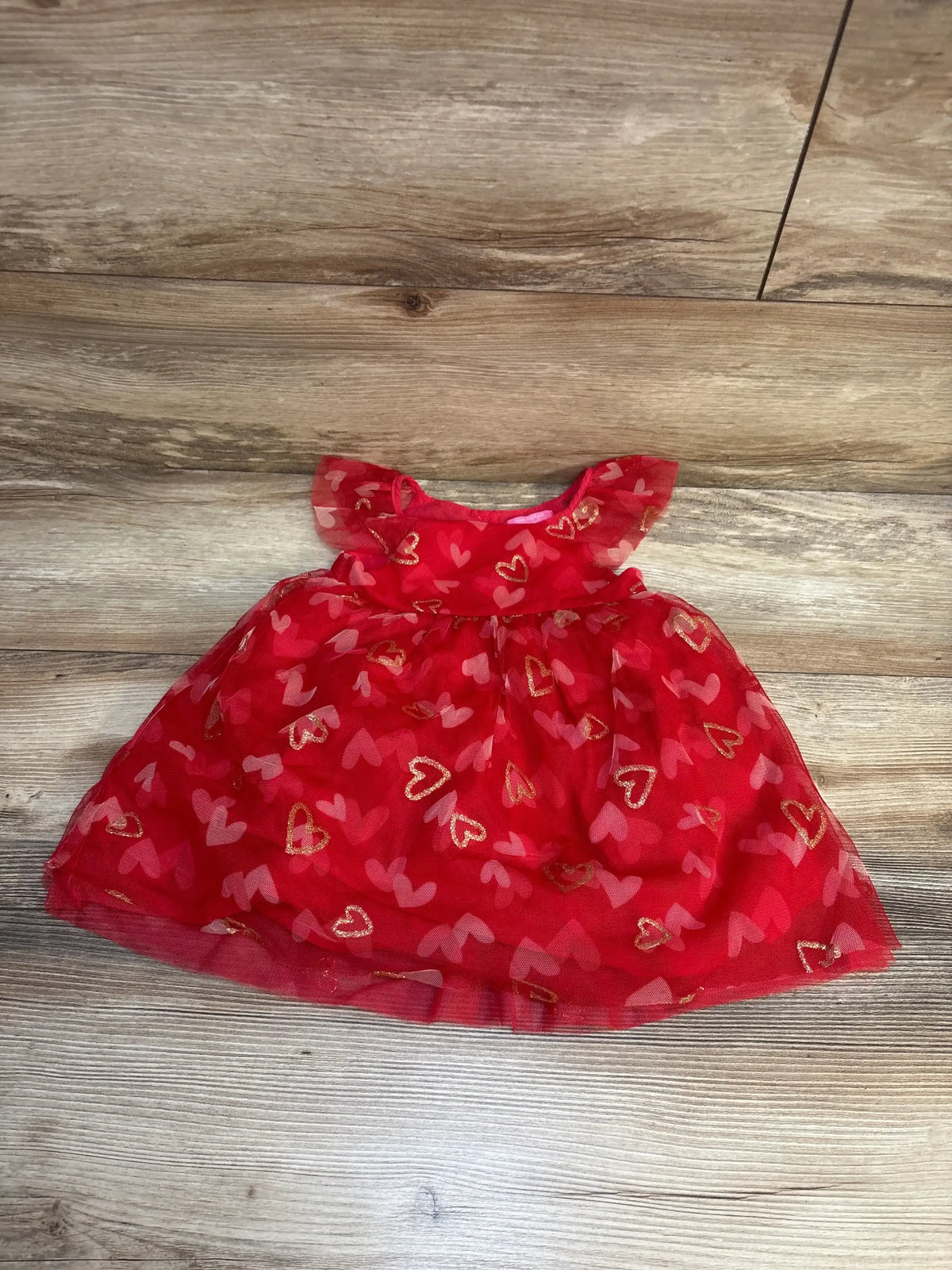Red baby dress with gold and pink heart patterns on wooden floor