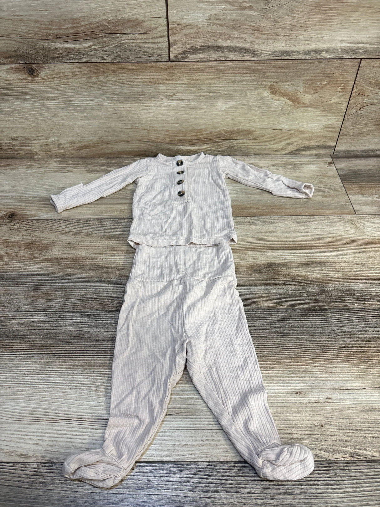 Top-down view of Lou Lou Cove ribbed 2pc newborn set in beige with front buttons and vertical rib texture on wood floor