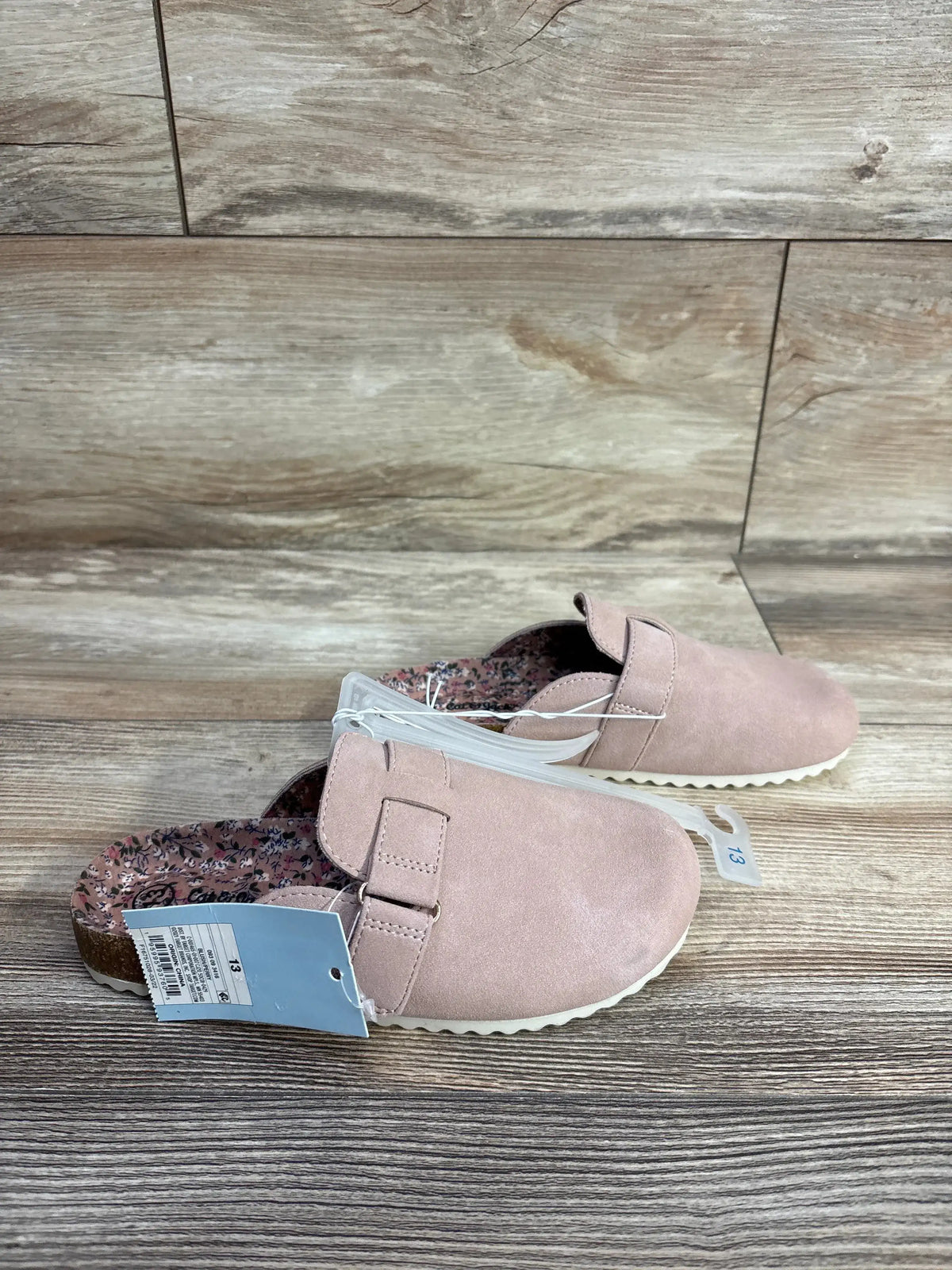Pair of pink children's slip-on shoes with floral inner lining and size 13 tag on wooden floor