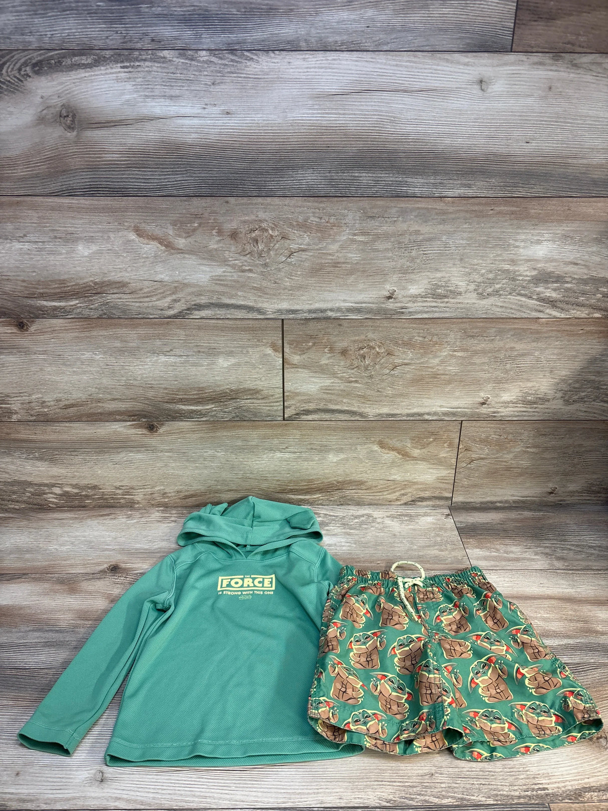 Green kids hoodie and Baby Yoda print shorts laid flat on wood background