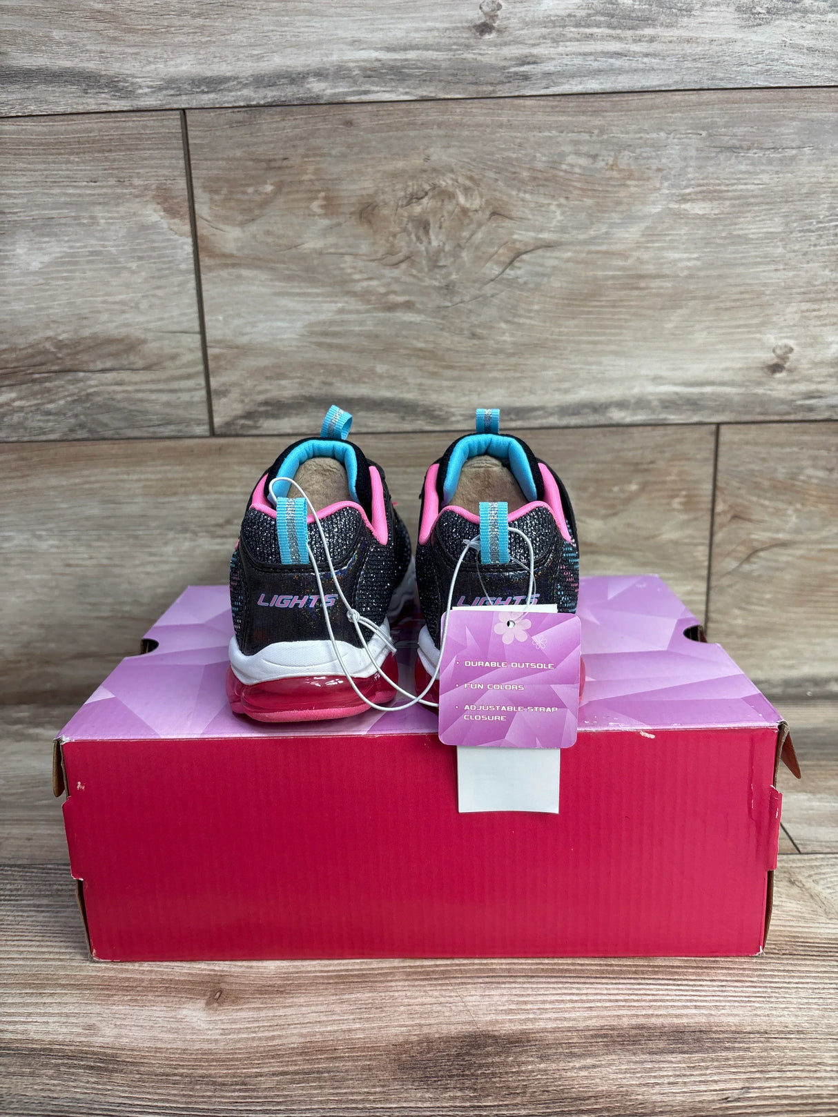 Kids black and pink Skechers Lights sneakers with blue accents on pink shoebox with wood background