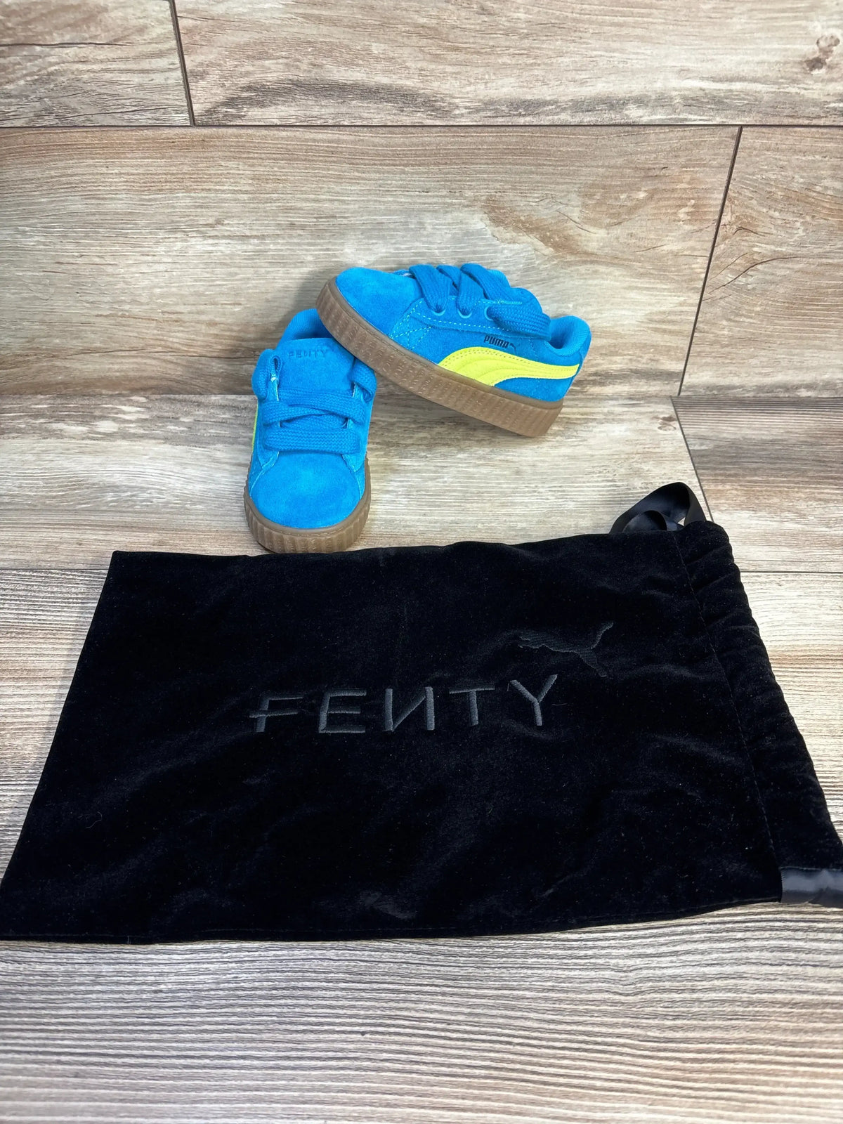 Blue and yellow Puma Fenty toddler sneakers with black Fenty dust bag on wood floor