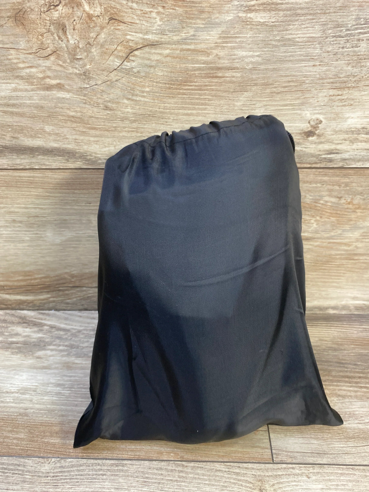 Front view of Cozybonder toddler airplane seat extender folded inside a black drawstring storage pouch on wood background