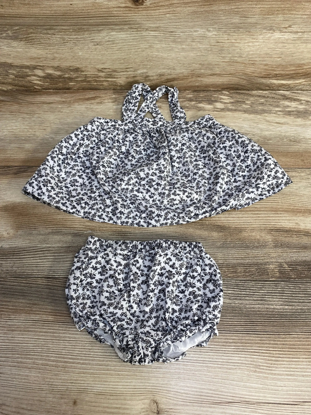 Flat lay of Janie and Jack white ditsy floral 2-piece set showing strappy top and elastic-waist bloomers on wood background