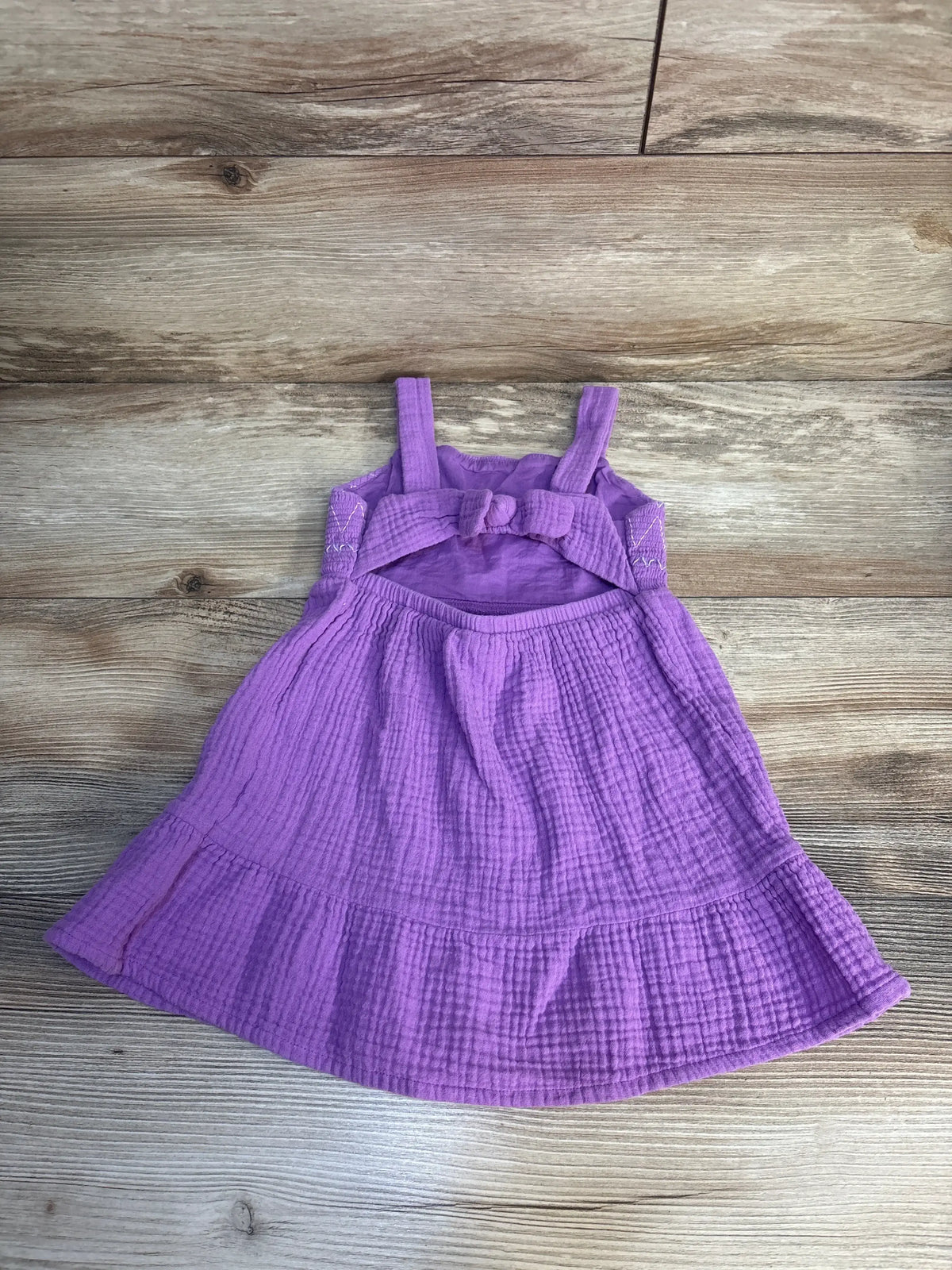 Purple toddler sundress with bow detail and textured fabric on wood background