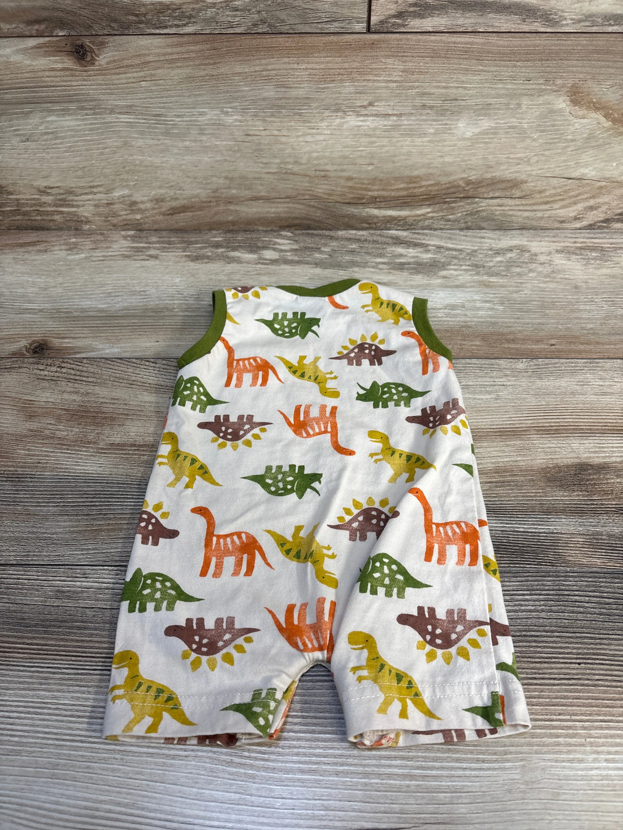 Baby dinosaur print romper with colorful T-Rex, Stegosaurus, and Triceratops on white, green trim, wood background