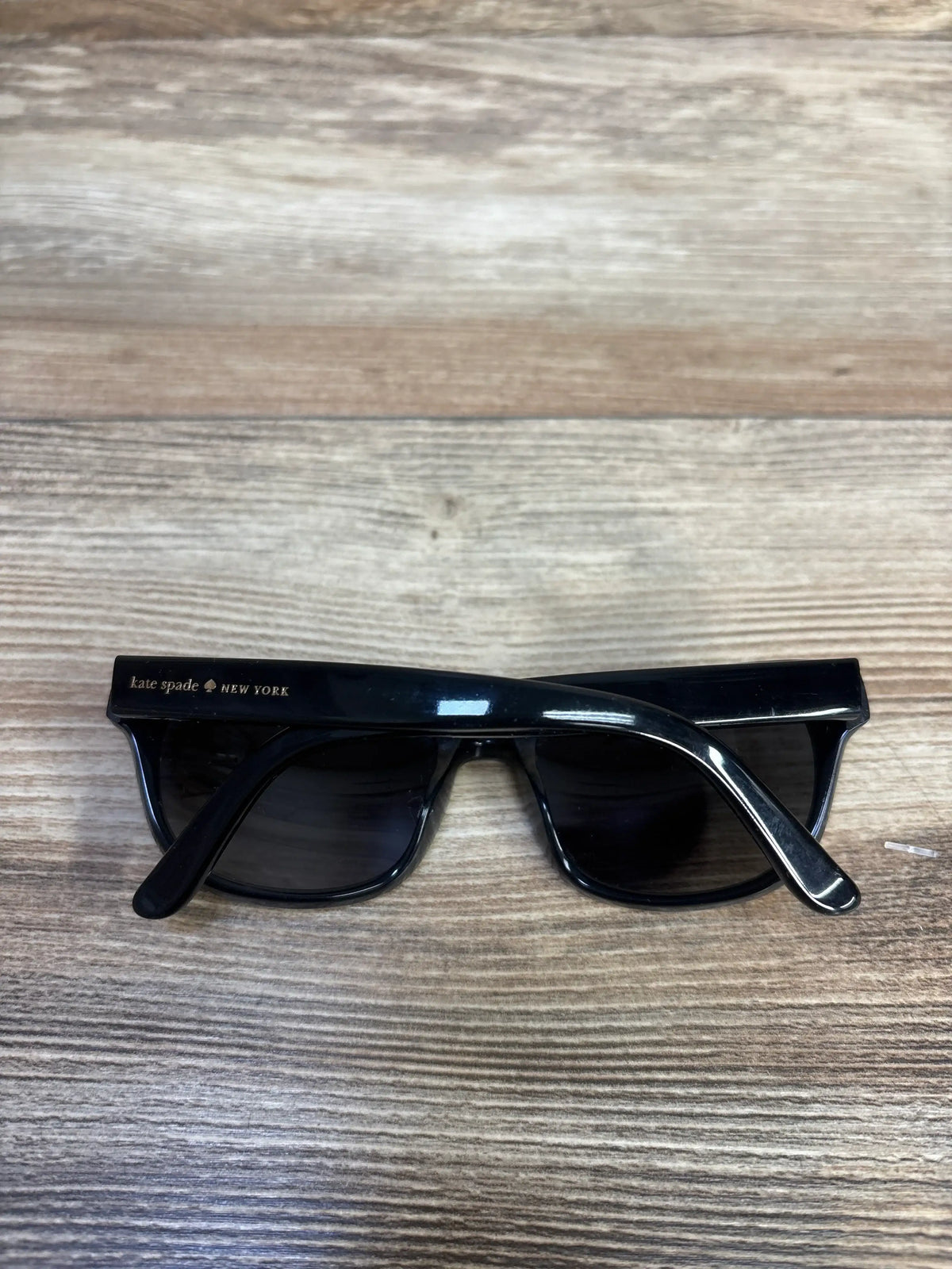 Front view of Kate Spade New York Tamsin/S sunglasses showcasing black rectangular plastic frames and dark lenses on a wood-grain surface