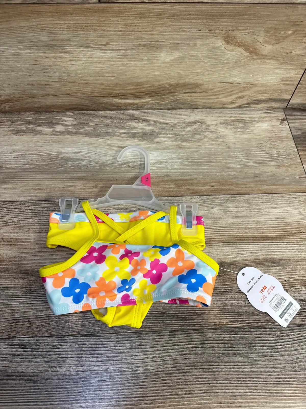 Flat view of Wonder Nation 2pc swimsuit in size 18M showcasing yellow trim and colorful floral print on wood grain