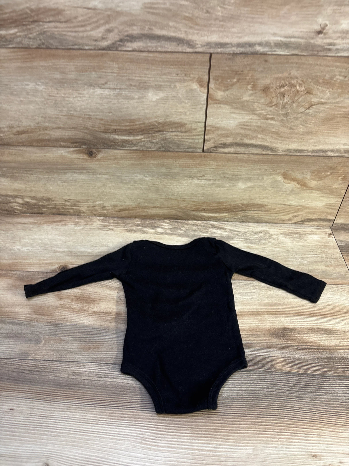 Flat lay of Jordan black long-sleeve baby bodysuit (12 months) showcasing long sleeves and snap closure with wood background