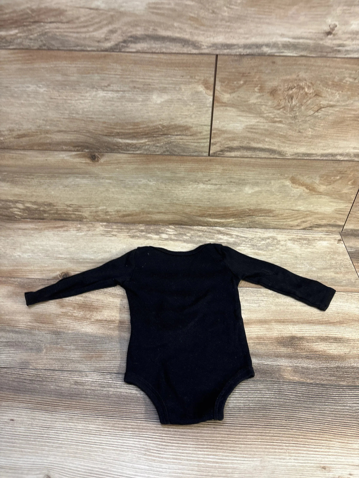 Flat lay of Jordan black long-sleeve baby bodysuit (12 months) showcasing long sleeves and snap closure with wood background