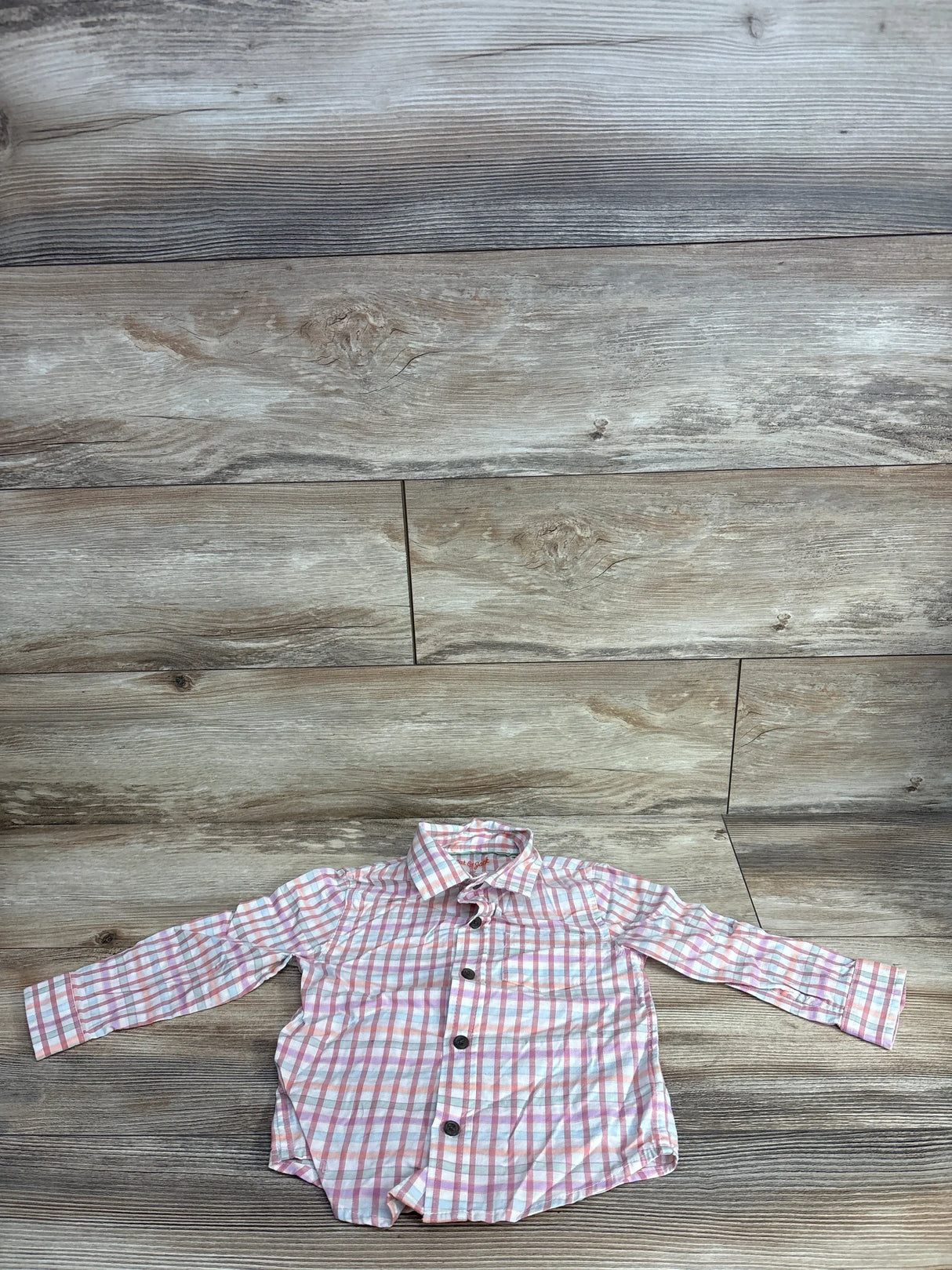 Long sleeve pink and white plaid button-up toddler shirt on wood background