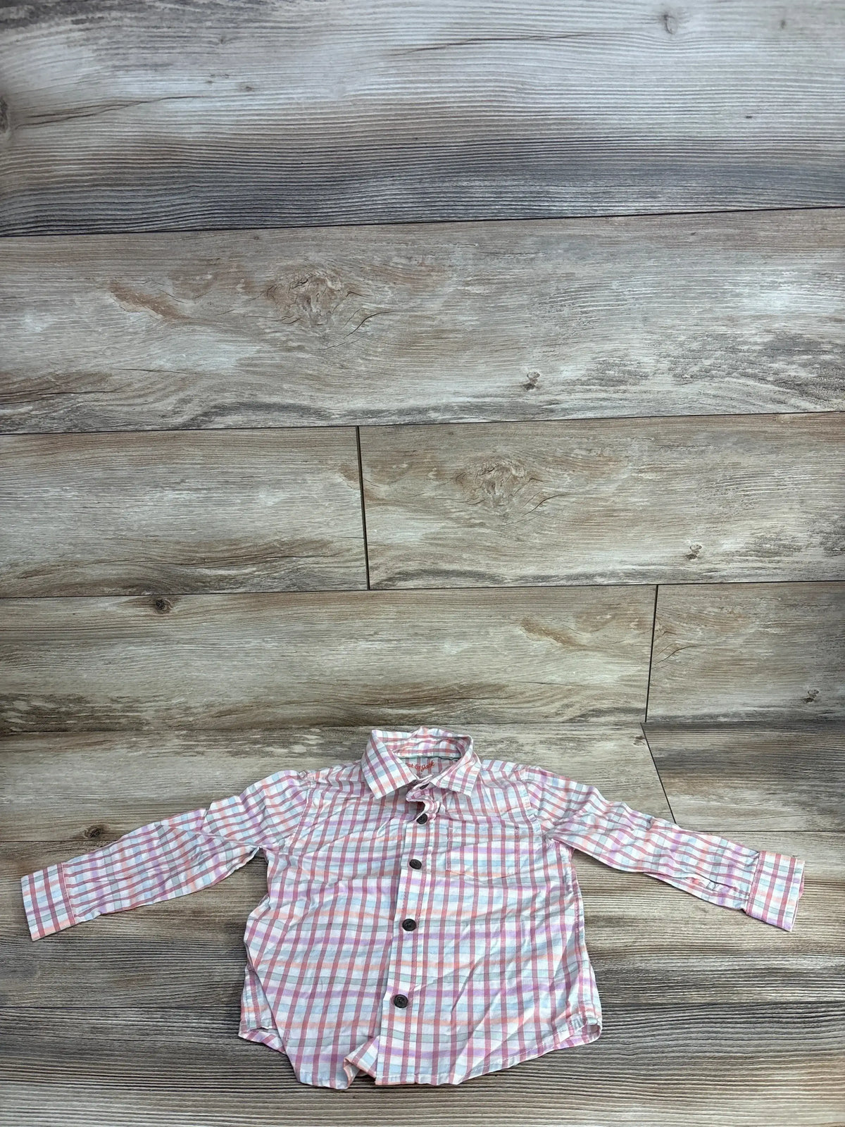Long sleeve pink and white plaid button-up toddler shirt on wood background