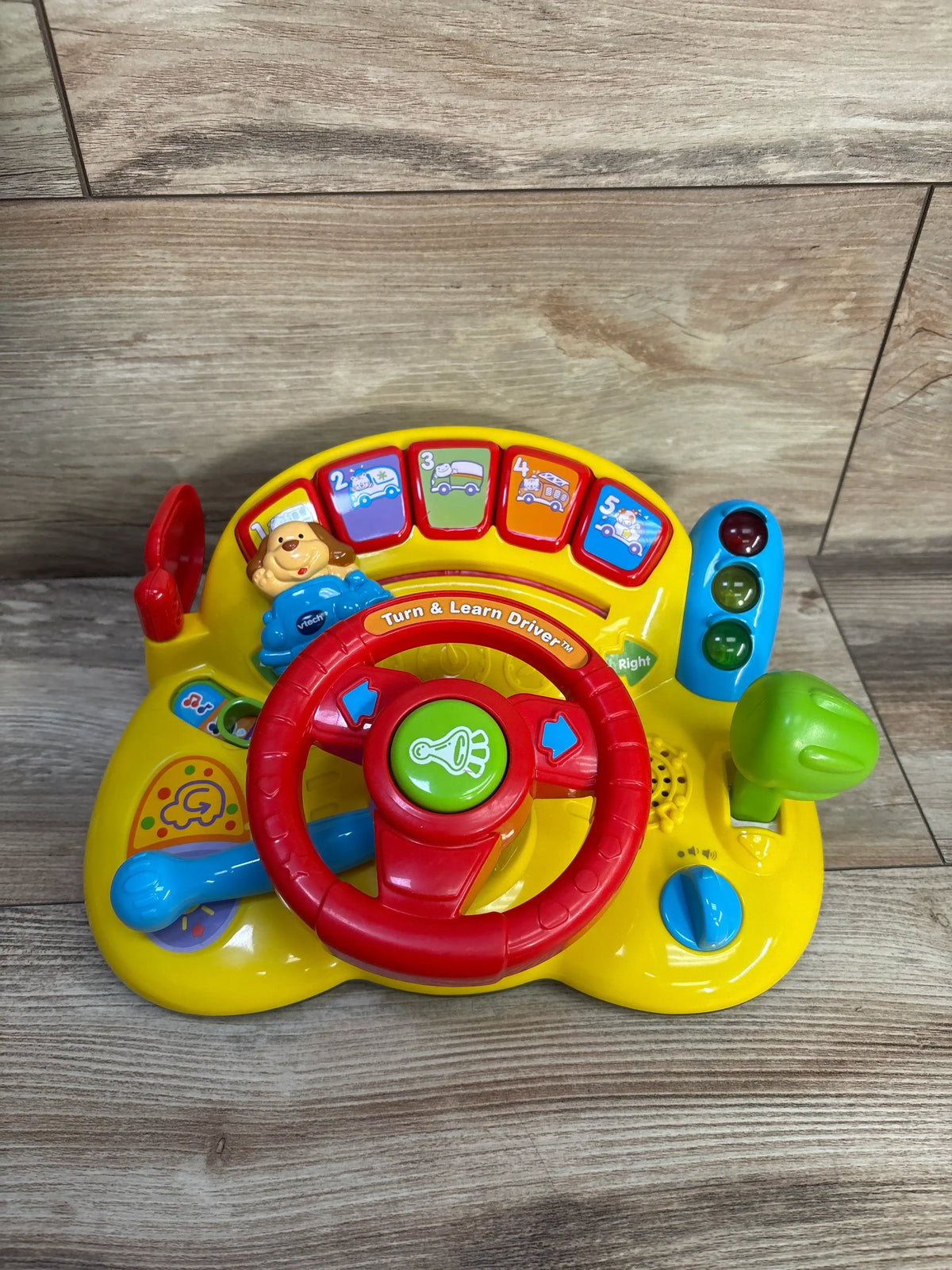 Front view of Vtech Turn & Learn Driver with steering wheel, gear shifter, buttons, and traffic lights on wood floor