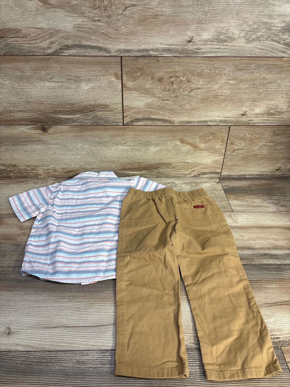 Flat lay of a Wrangler toddler white button-up shirt and matching shorts showcasing the coordinated set on a wood-look background