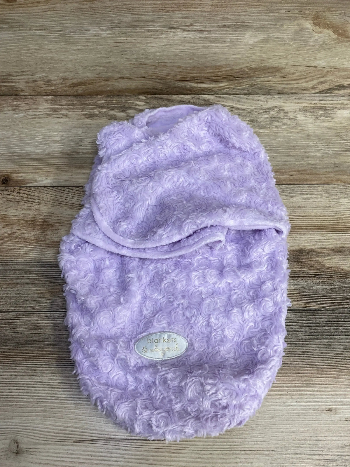 Soft lavender baby swaddle blanket with textured swirl pattern and label on wooden background