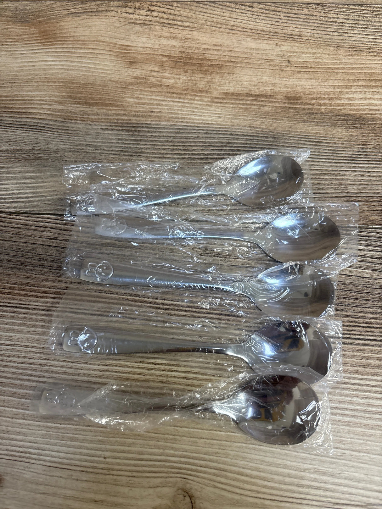 Four individually wrapped stainless steel spoons on wood grain surface