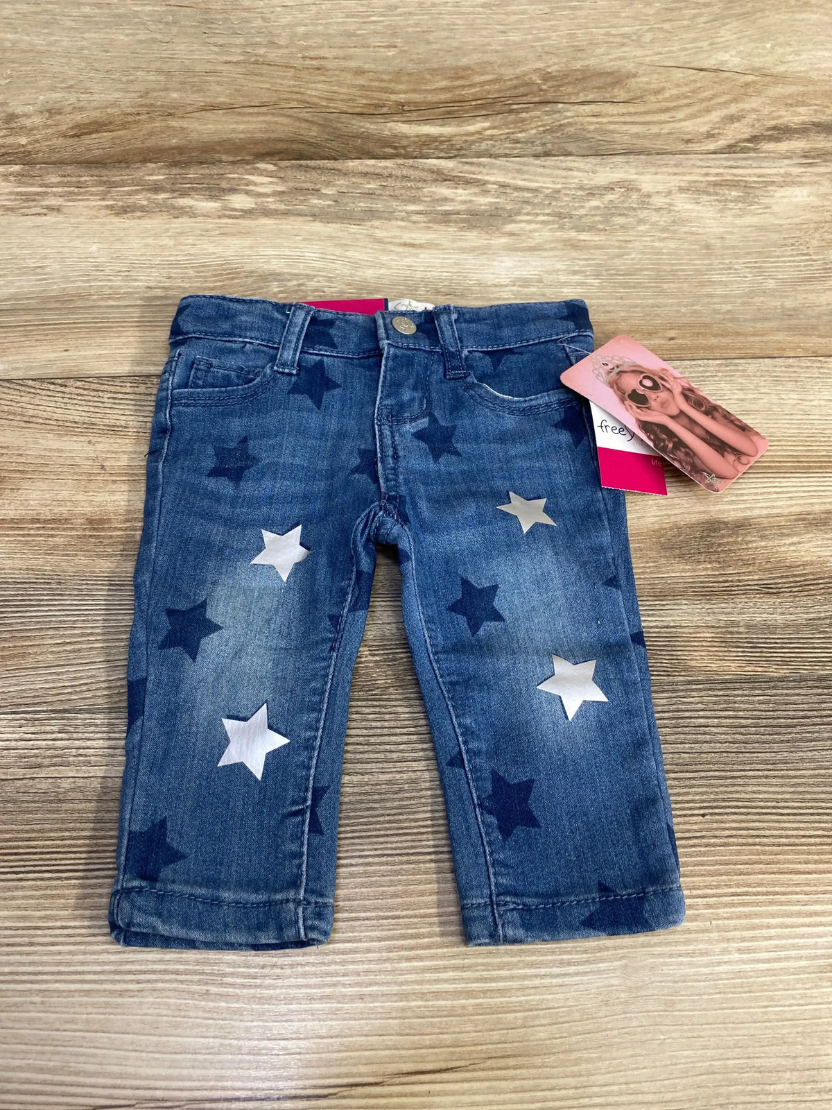 Flat lay of newborn blue star-print jeans showing silver and navy stars, front pockets and waistband on wood background