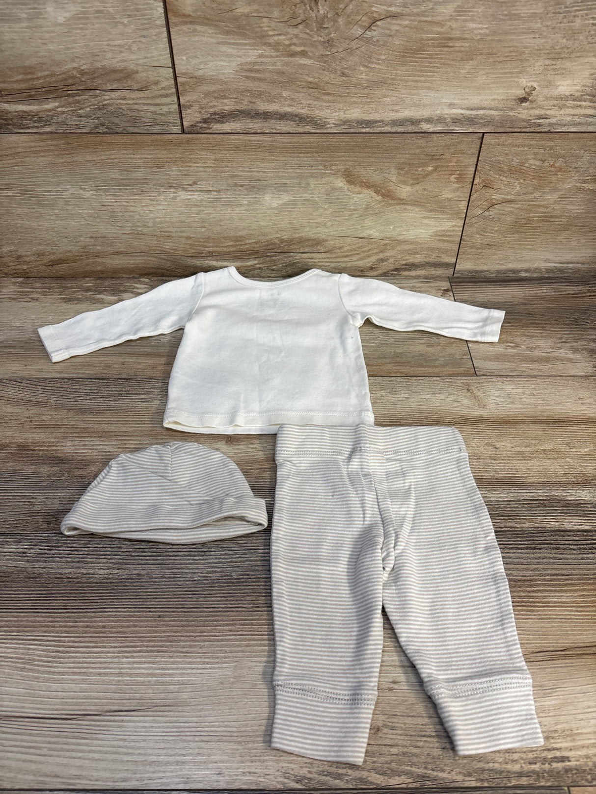 White baby long sleeve top, striped pants, and hat set on wood floor