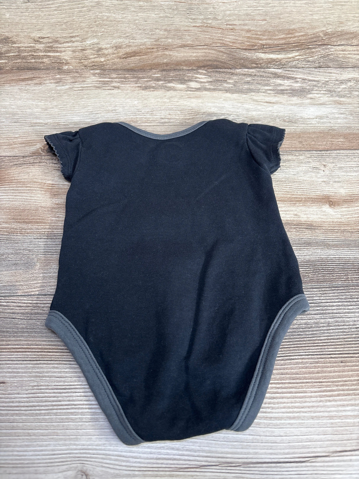 Black baby onesie with grey trim laid flat on wooden surface