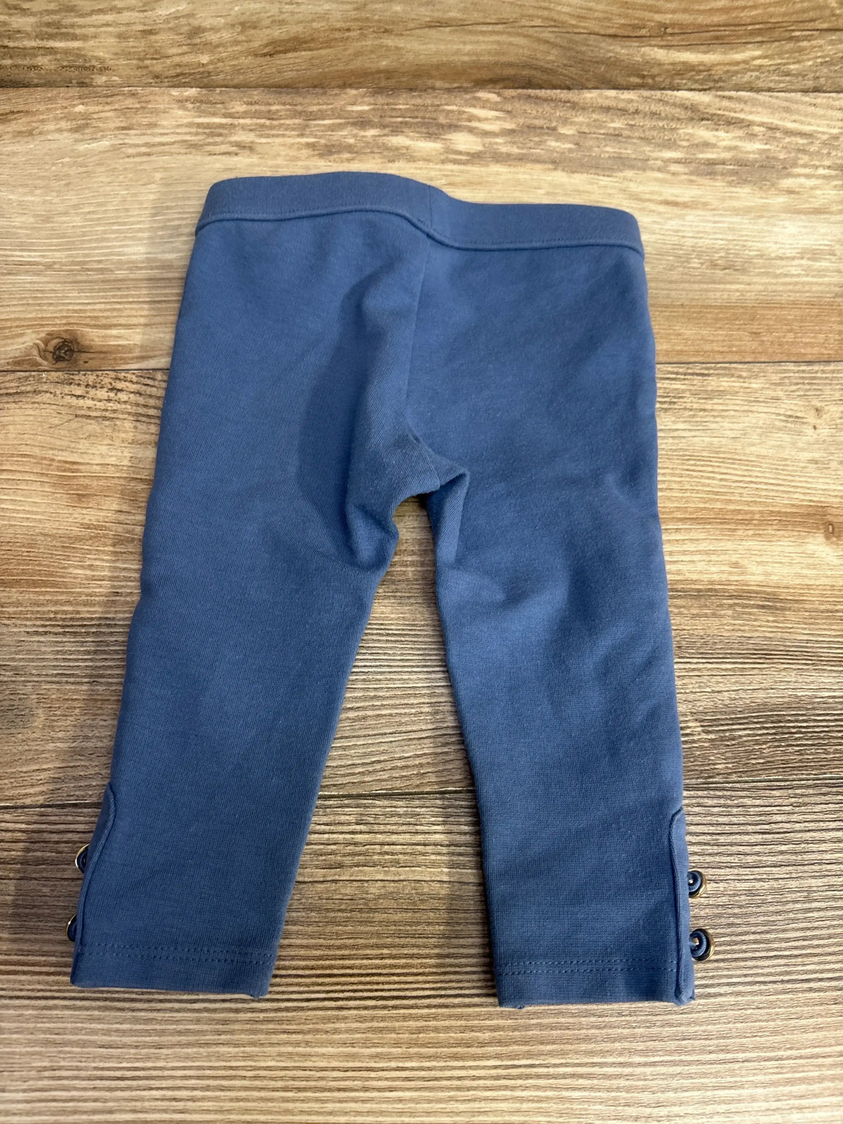 Flat lay of Janie & Jack River Run blue ponte pant, size 6-12m, showing gold-tone button cuffs and elasticized waist on wood