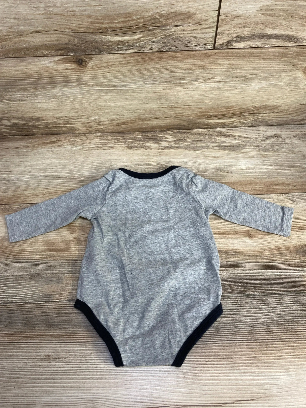 Flat lay back view of grey Nike long-sleeve baby bodysuit size 3-6 months showing black trim on wood background