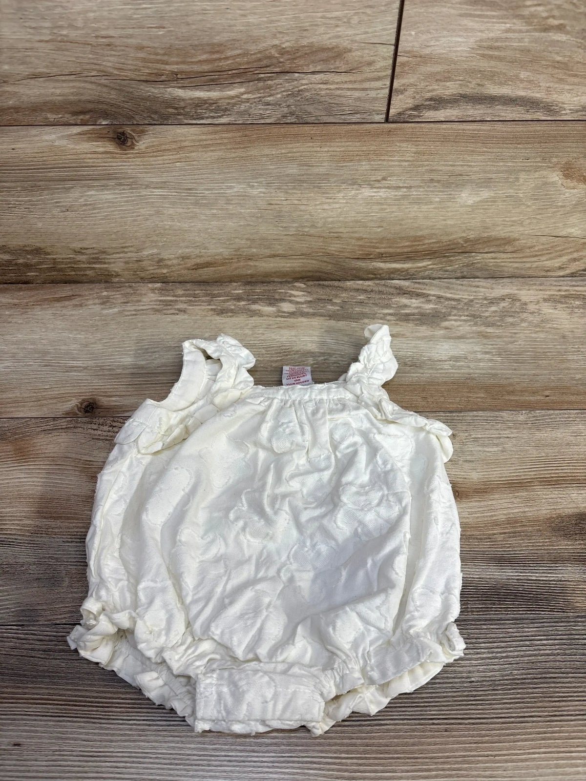 Front view of Haute Hippie bubble romper showcasing ivory cotton with ruffled tank straps and elasticized leg openings on wood plank floor