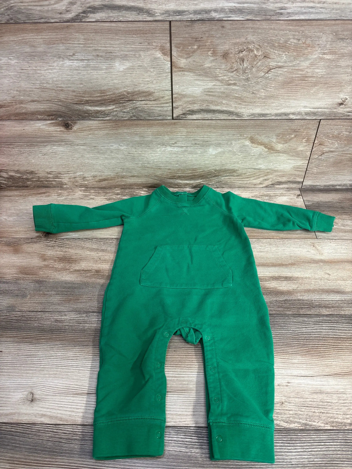 Green long sleeve baby romper with front pocket and snap leg closures on wooden floor