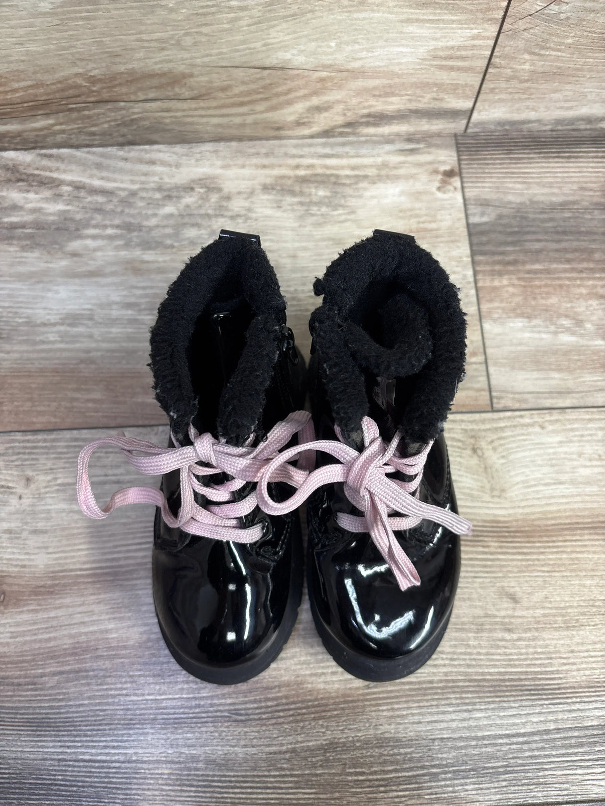 Pair of black shiny toddler boots with pink laces and fuzzy lining on wooden floor