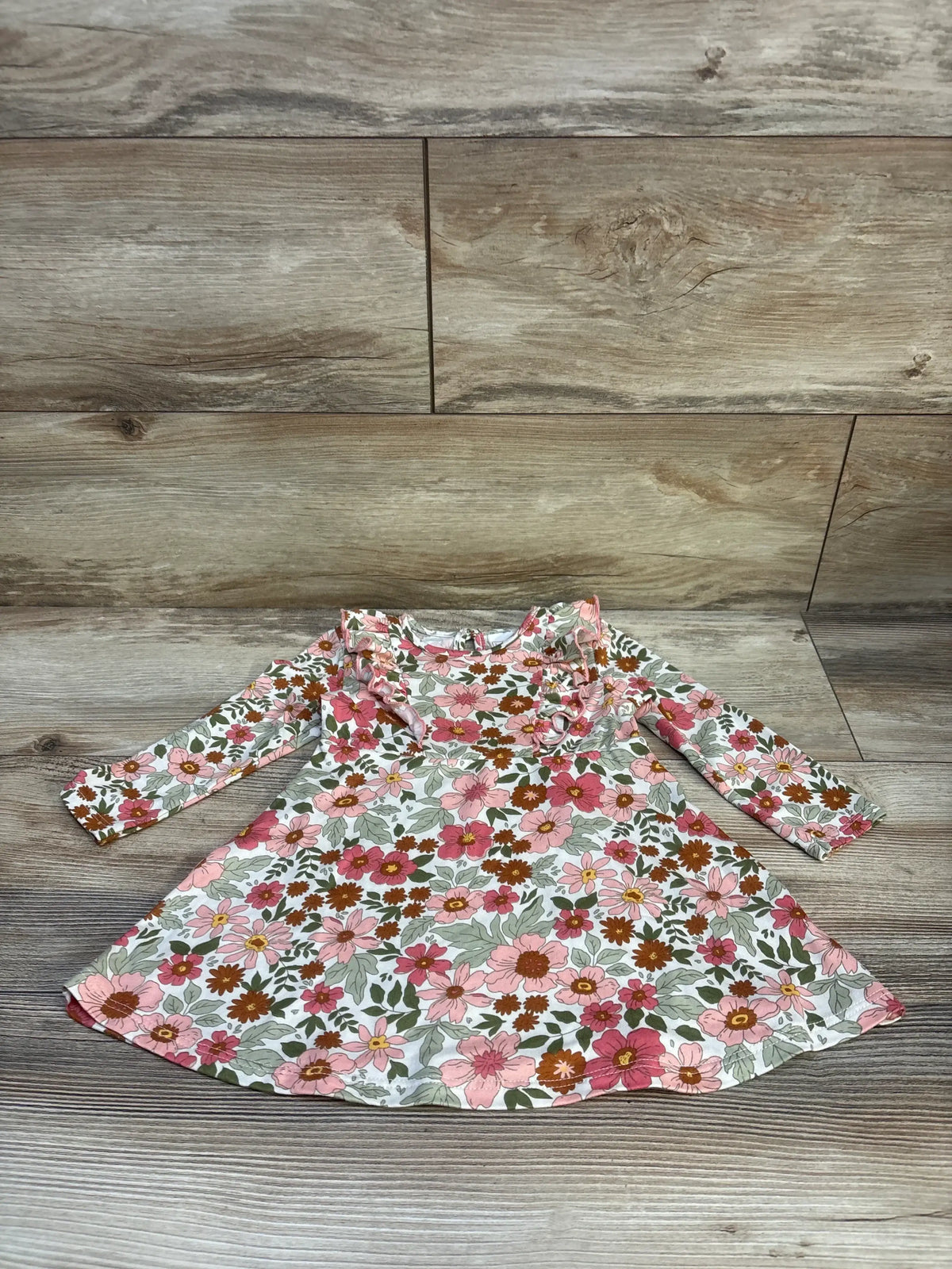 Flat lay of girls’ long-sleeve floral dress showcasing ruffle neckline and pink and brown flower print with wood plank background