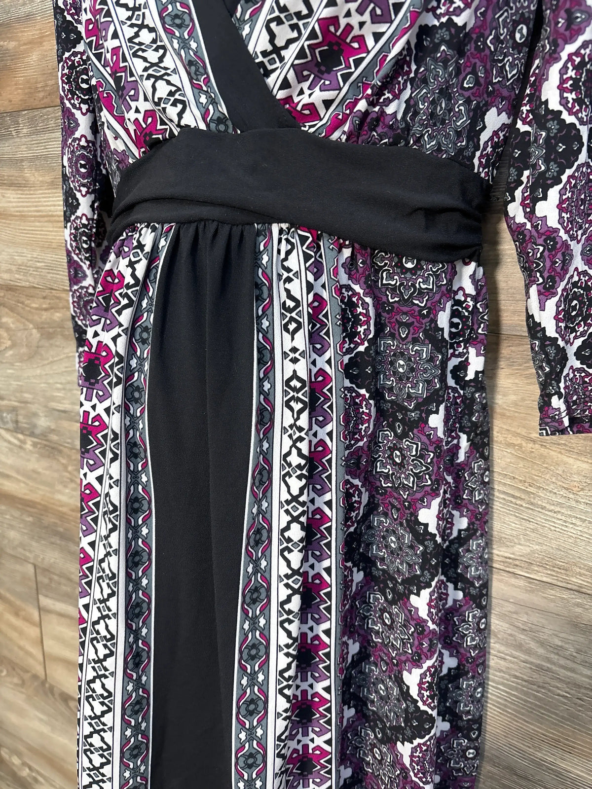Close-up front view of Motherhood Maternity geometric long sleeve maternity dress in purple, showing V-neck and black waist panel on wood floor