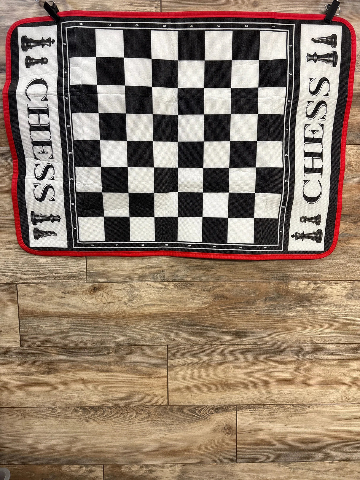 Top down view of EasyGo chess mat 3 by 4 feet showing checkerboard squares, red border and CHESS lettering on wood floor