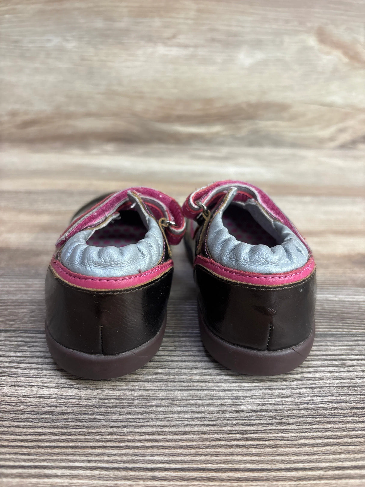Rear view of Robeez faux leather Mary Jane sneakers in brown showcasing pink trim and gray padded cuffs on a wooden surface