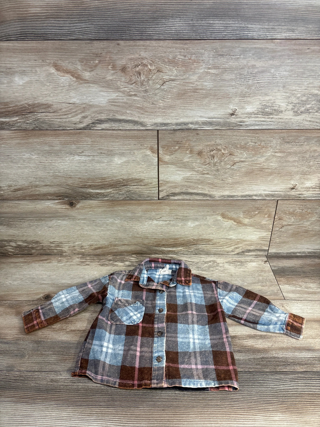 Children's long-sleeve plaid button-up shirt with brown, blue, and pink checks on wooden floor