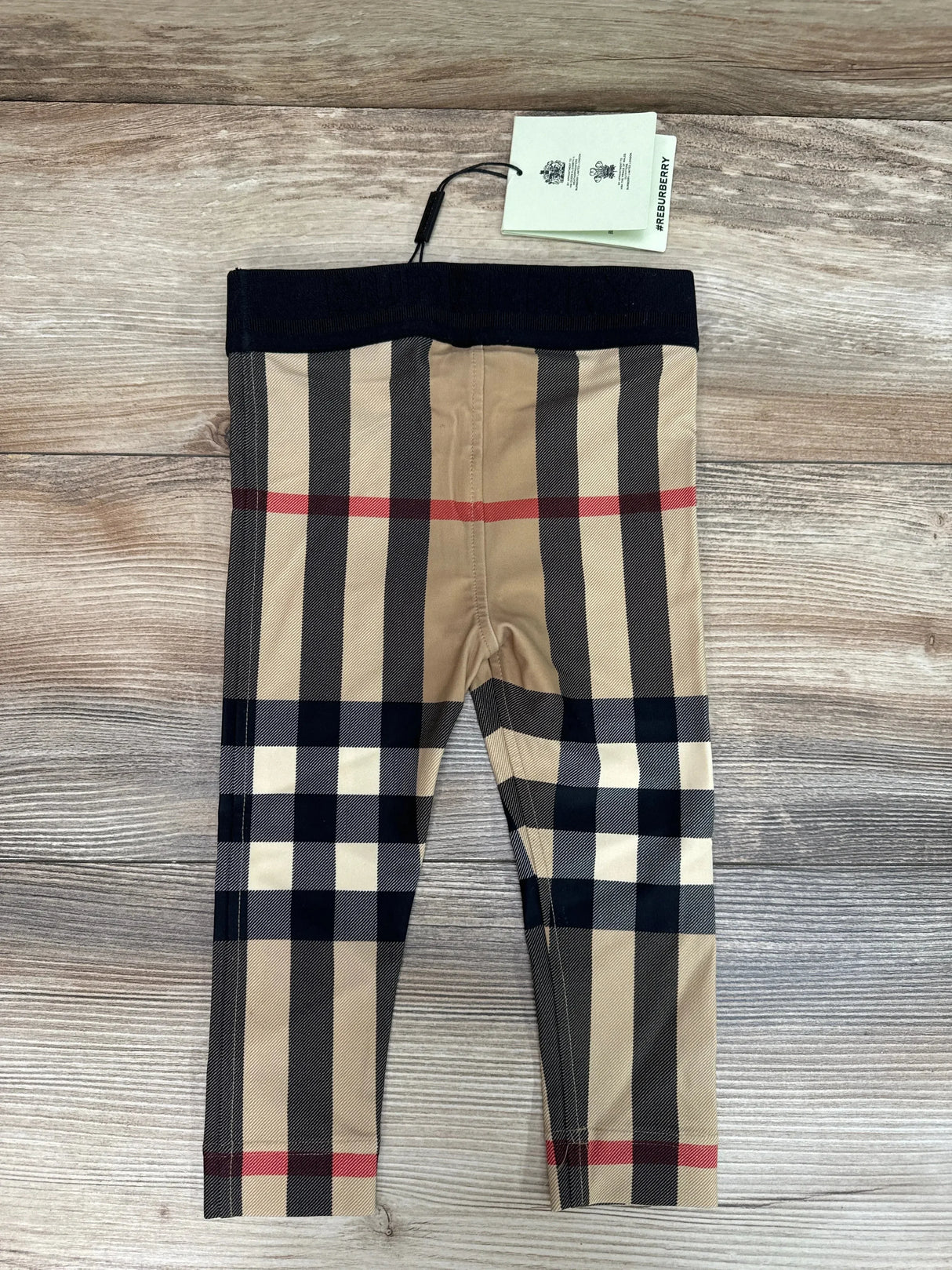 Flat-lay of Burberry beige Gina check baby leggings size 18 months with black elastic waistband on light wood floor