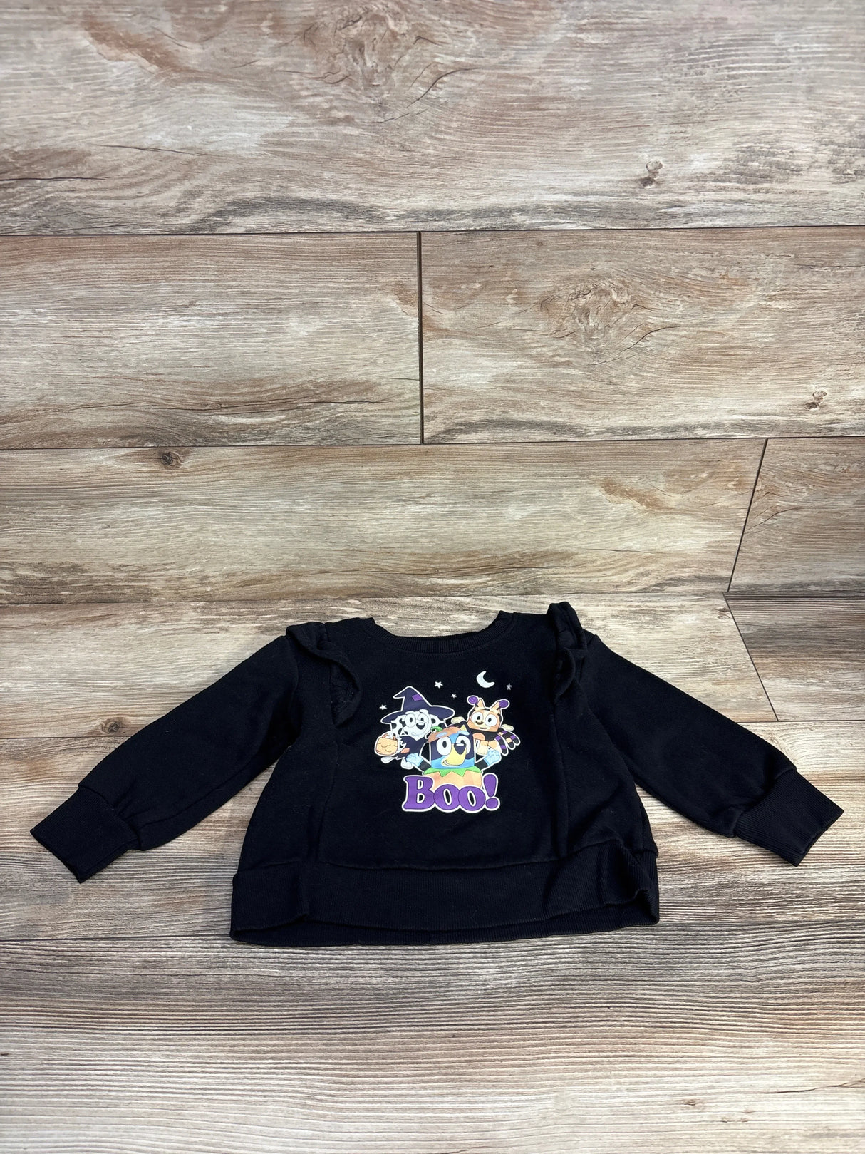 Black kids Halloween sweatshirt with Boo graphic and ruffled sleeves on wood floor