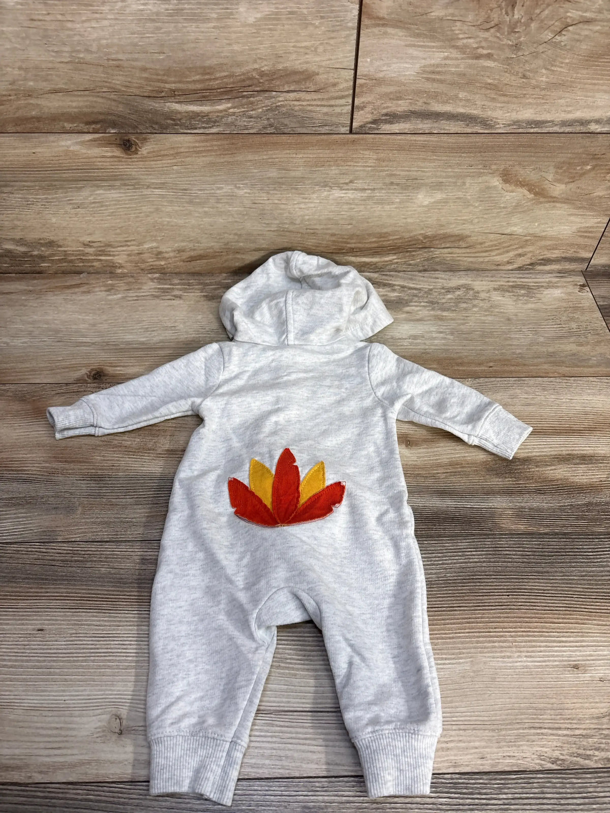 Gray baby onesie with hood and autumn leaf appliqué, laid on wood floor