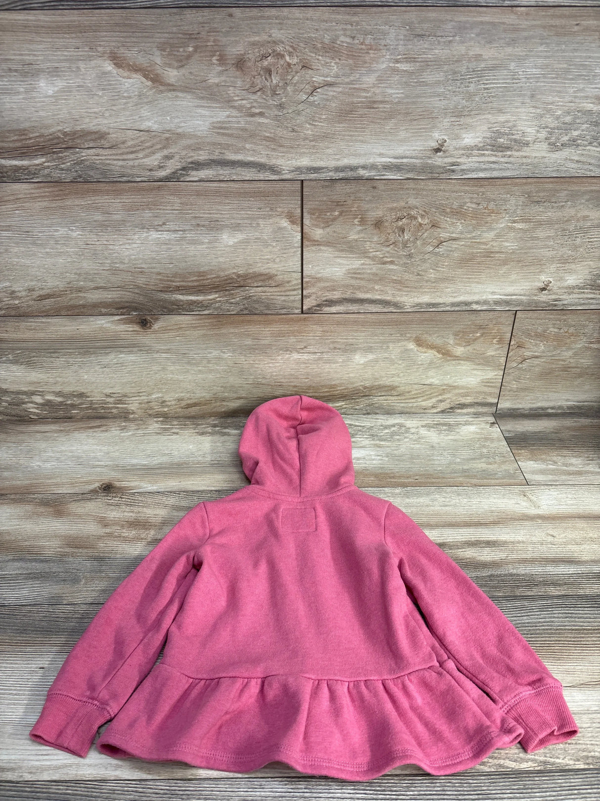 Back view of a pink toddler hoodie with long sleeves and ruffled hem on wooden floor
