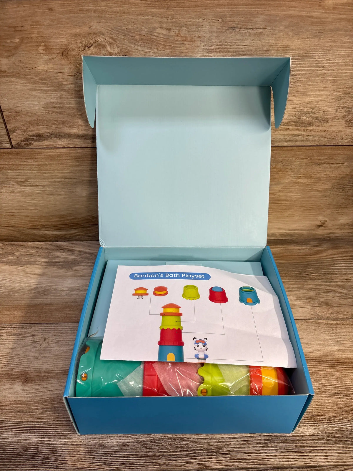 Top view of NEW Banban’s Bath Play Set showcasing lighthouse pieces and floating figures in an open box on a wood table