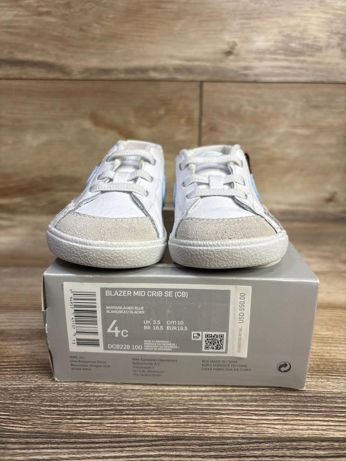 White and glacier blue Nike Blazer Mid Crib SE toddler shoes on box with size 4C label, wooden background
