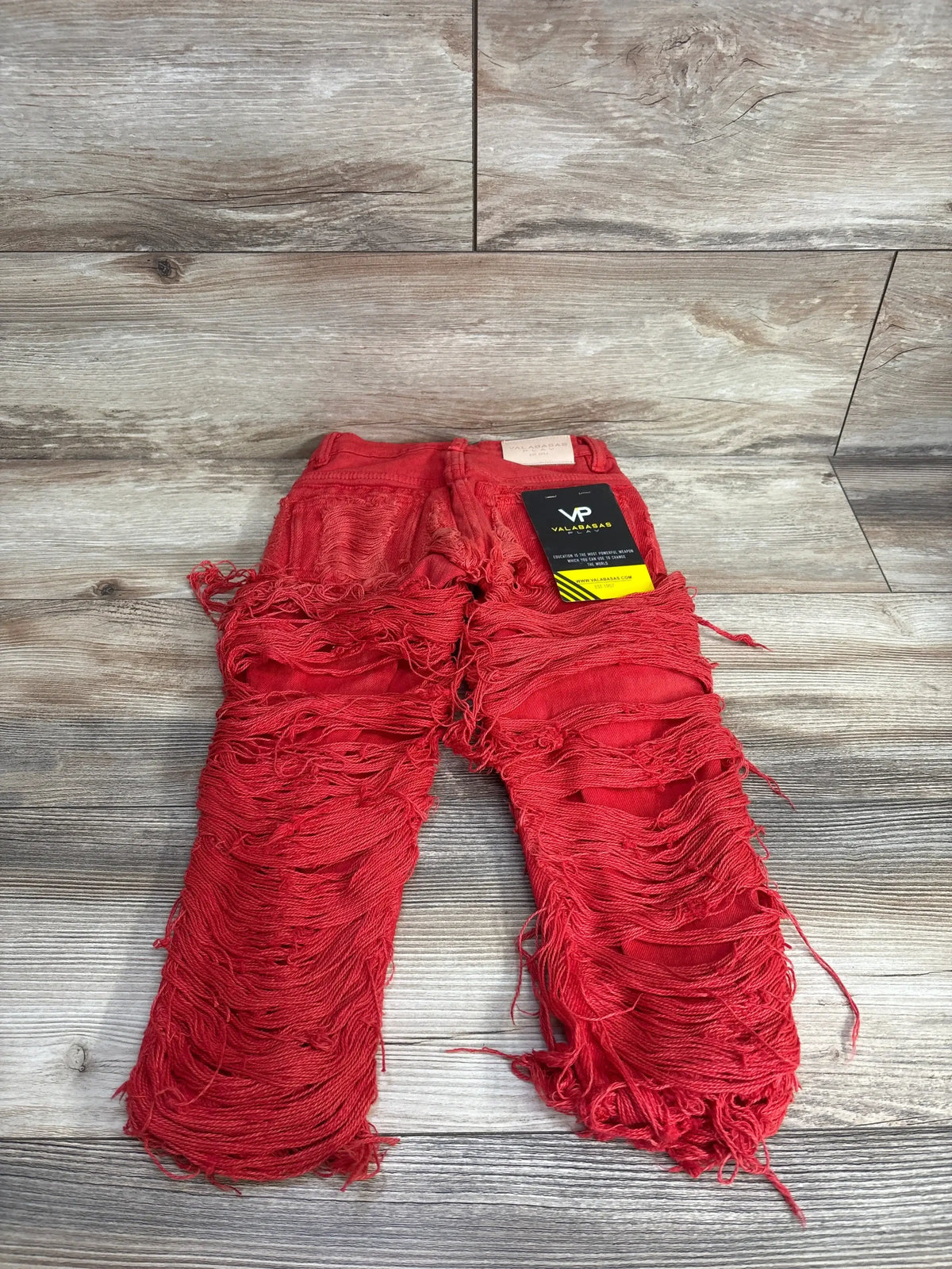 Red distressed fringe kids jeans with tag on wooden background
