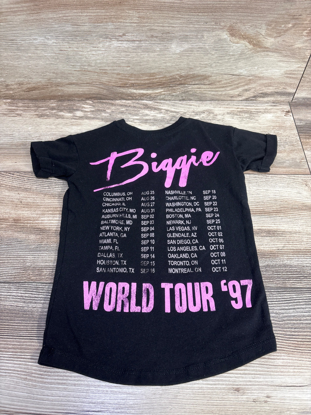 Black toddler-sized Biggie World Tour '97 t-shirt with pink lettering on wooden floor