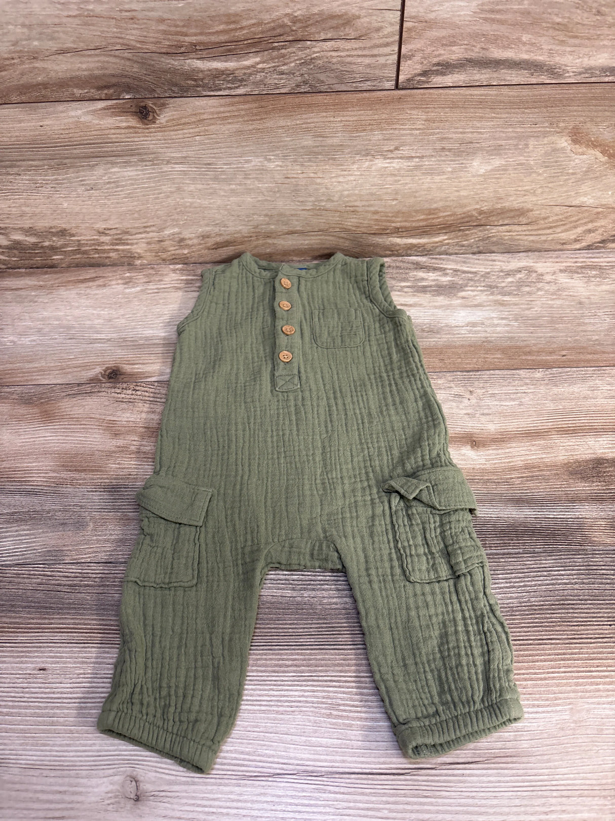 Flat lay of Old Navy olive green sleeveless henley jumpsuit with wooden buttons, chest and cargo pockets on wood floor