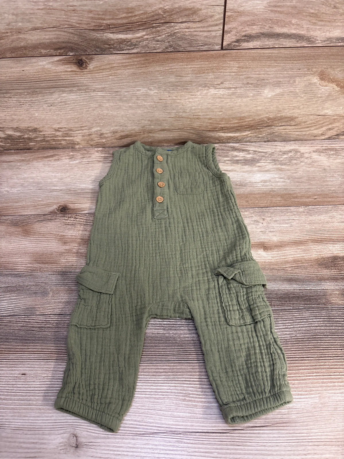 Flat lay of Old Navy olive green sleeveless henley jumpsuit with wooden buttons, chest and cargo pockets on wood floor