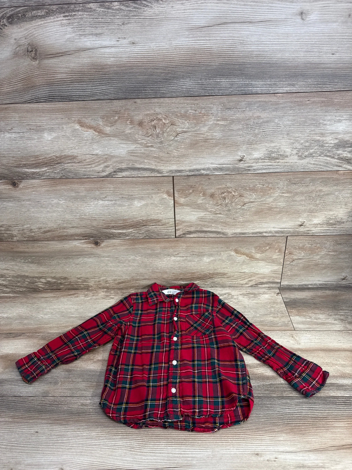 Red plaid long sleeve kids shirt with front pocket on wood background