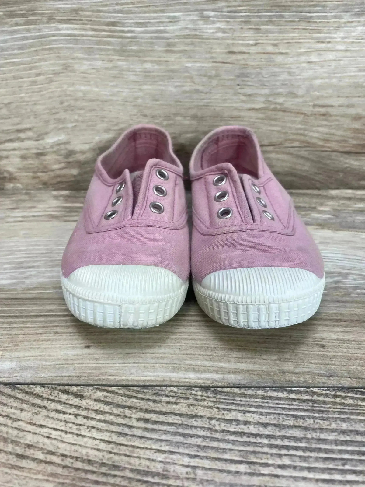 Front view of Cienta distressed pink canvas slip-on sneakers showcasing stretchy elastic and white rubber soles on wood grain