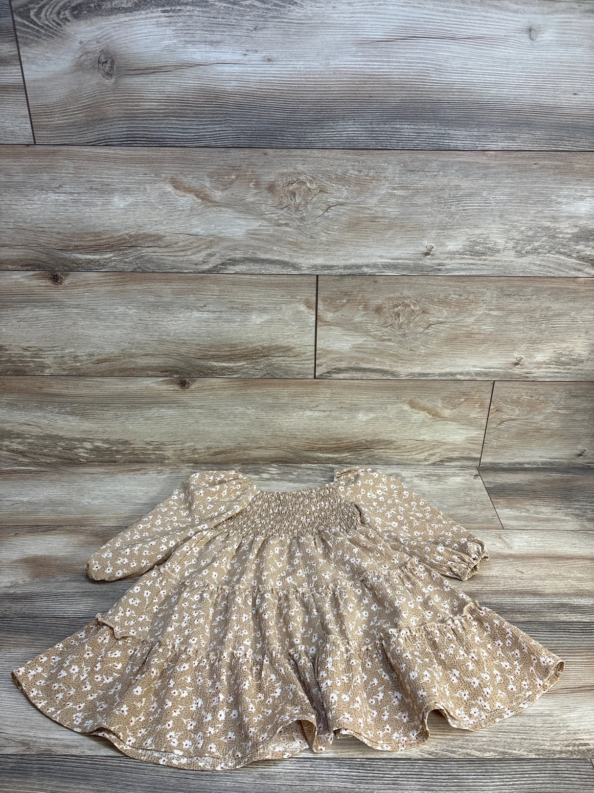 Tan floral baby dress with ruffles and long sleeves on wood floor