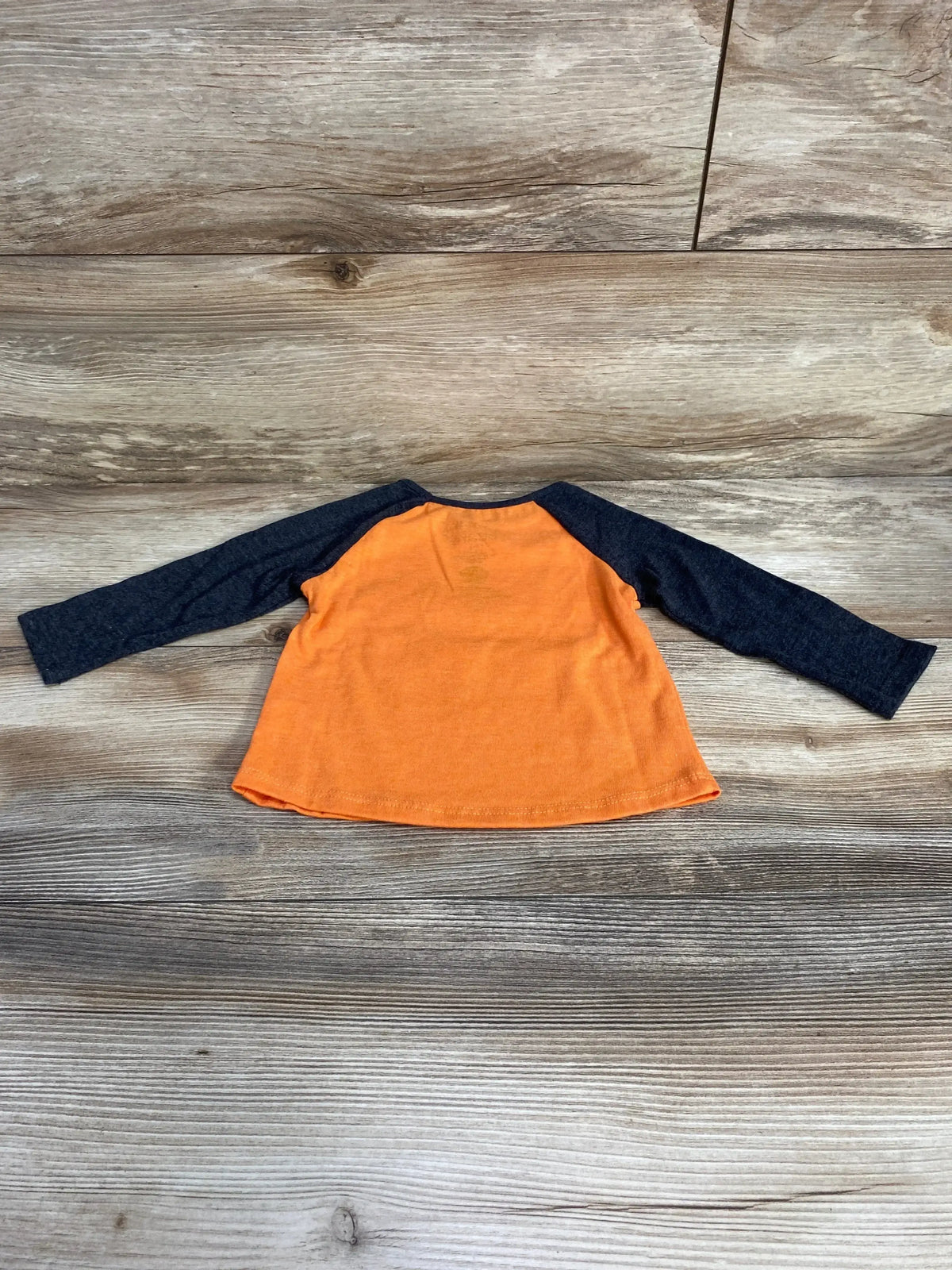 Back view of a Paw Patrol trick or treat shirt showcasing an orange body and dark navy raglan sleeves on a wood look floor