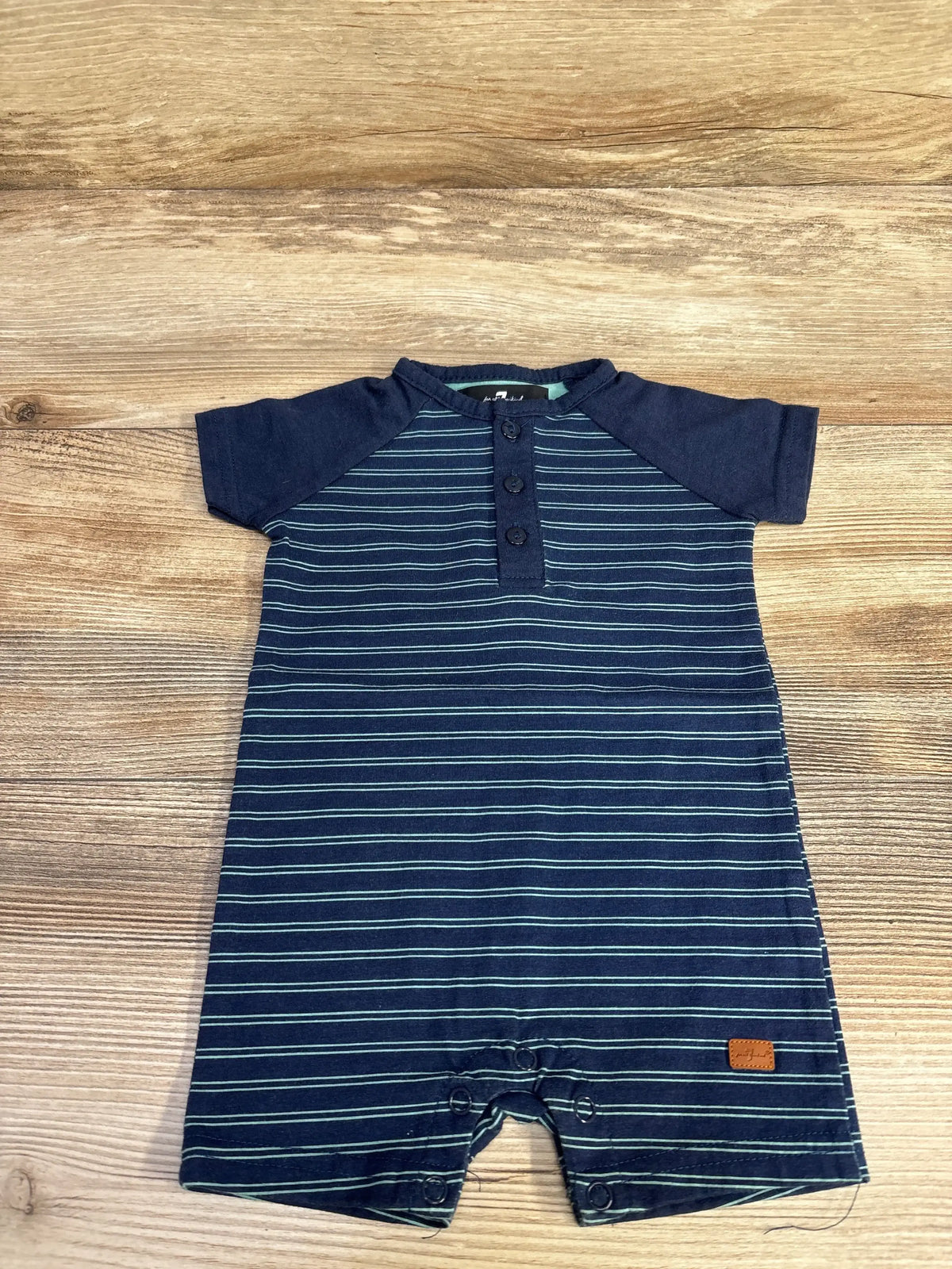 Flat lay of newborn striped Henley shortie romper showing three button placket and snap crotch on wood background