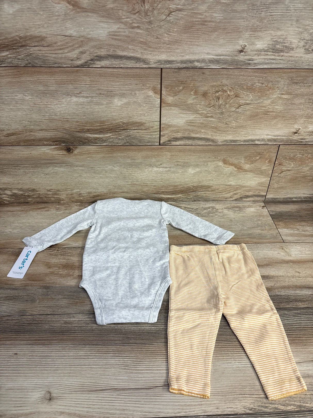 Gray baby long sleeve bodysuit with beige striped leggings on wood background