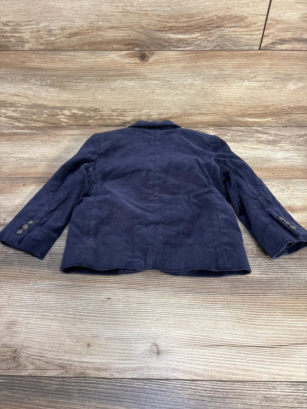 Back view of navy velvet toddler blazer, Janie & Jack size 2T, showing center seam and cuff buttons on wood background